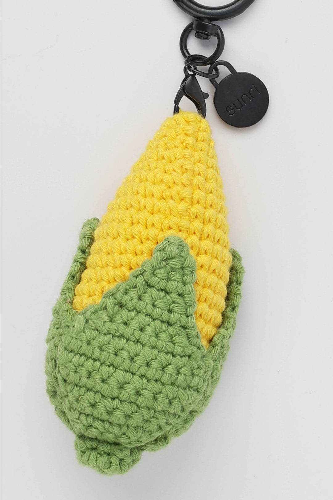 Crocheted corn on the cob keychain with a black metal clasp on a white background