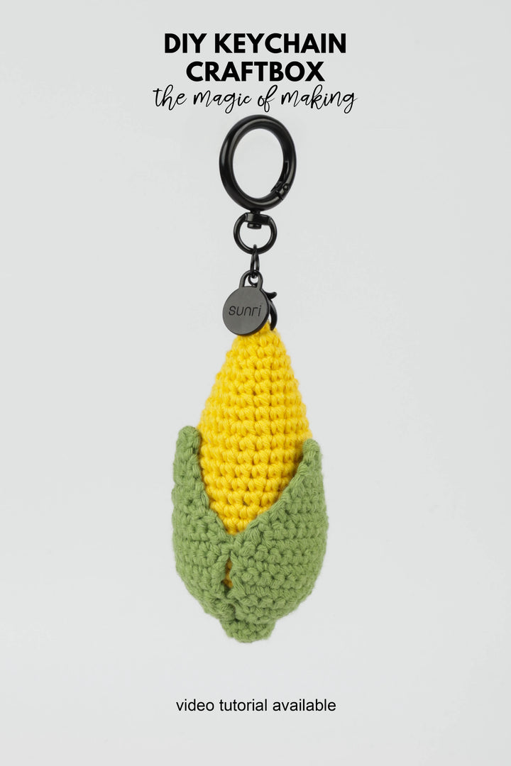 Crocheted keychain with yellow corn and green leaves on a white background, featuring text about DIY keychain craftbox.