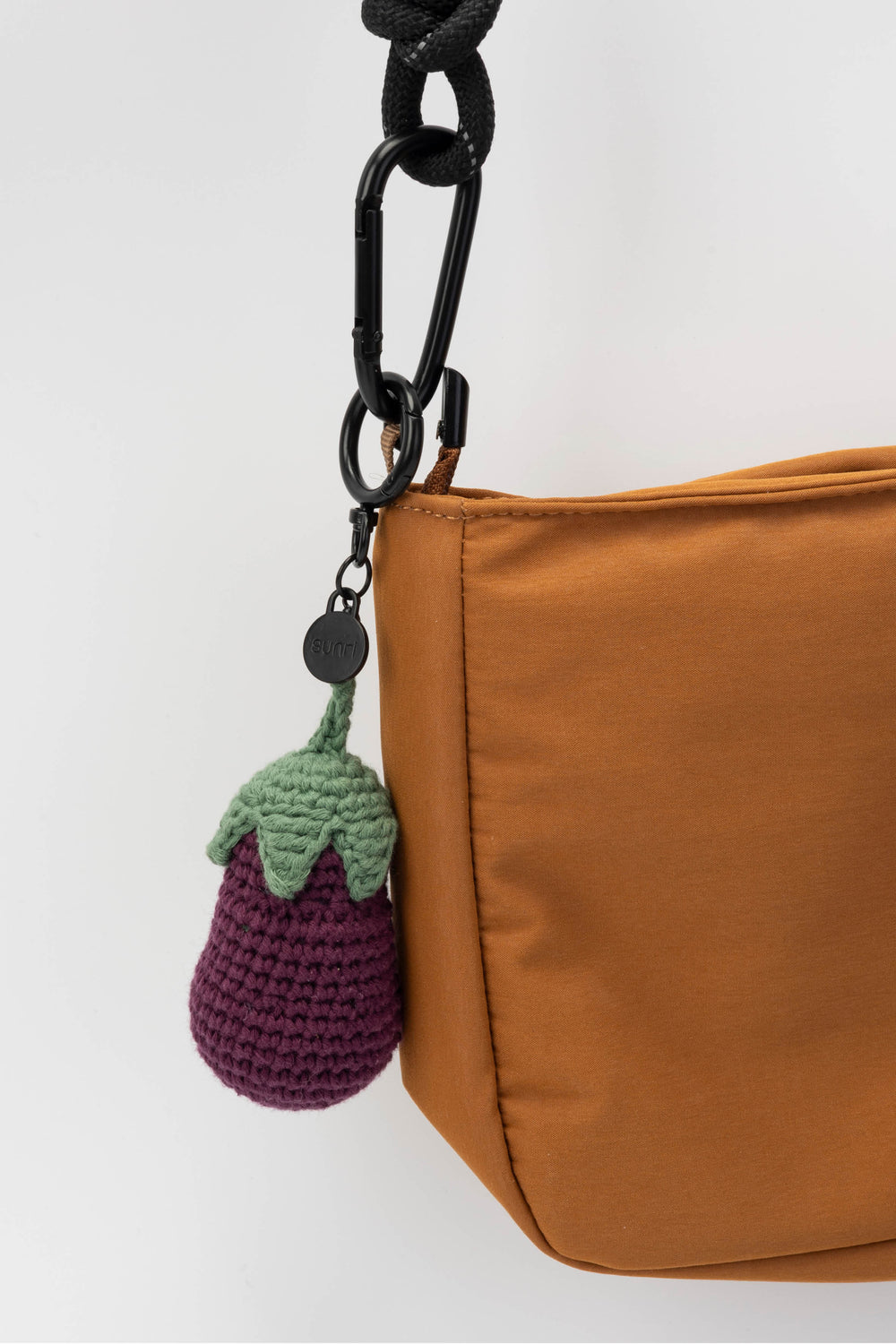 Brown bag with a purple and green crocheted eggplant charm on a white background