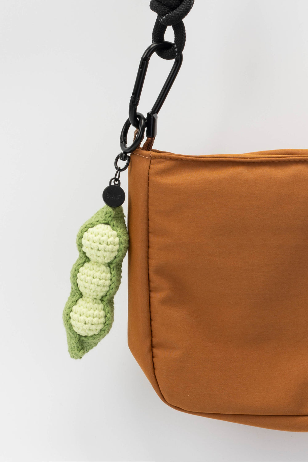Brown bag with a green crochet pea pod charm on a white background