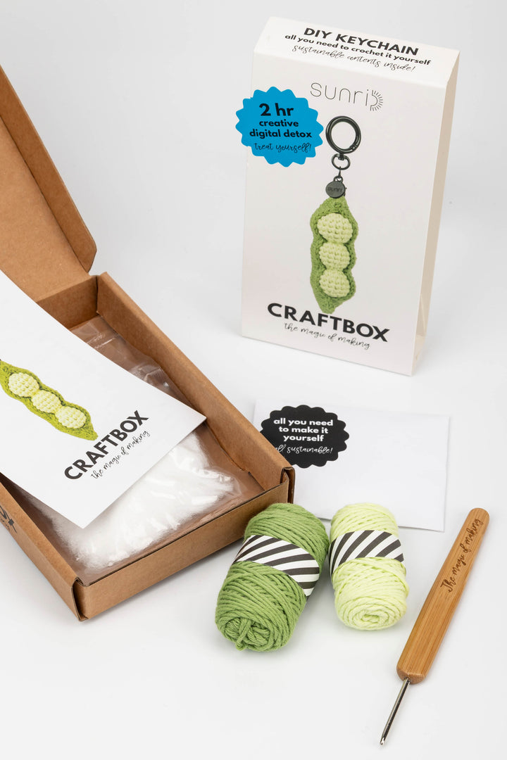 Craft kit with yarn, crochet hook, and keychain in a box on a white background