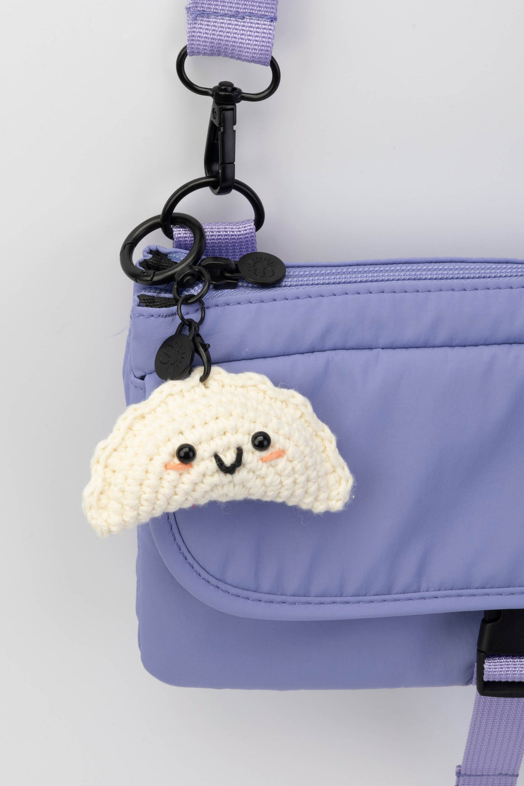 Gyoza-shaped keychain attached to a purple bag on a white background