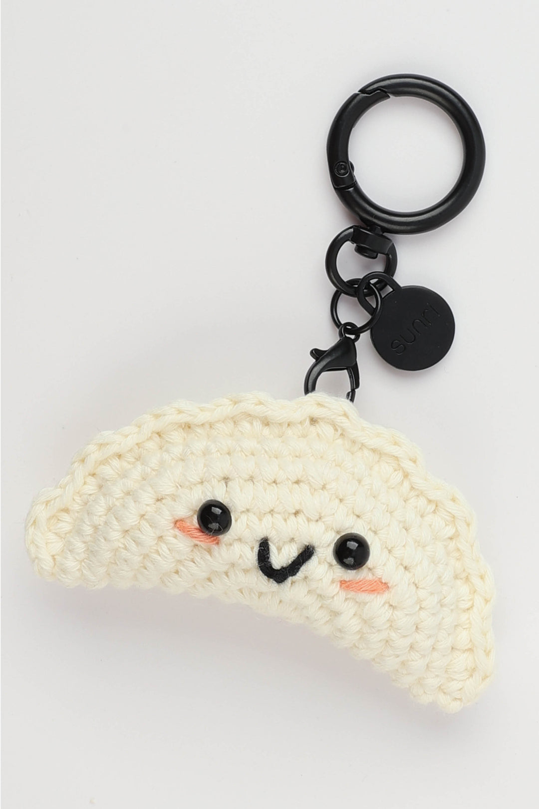 Crocheted Gyoza-shaped keychain with a face on a light gray background