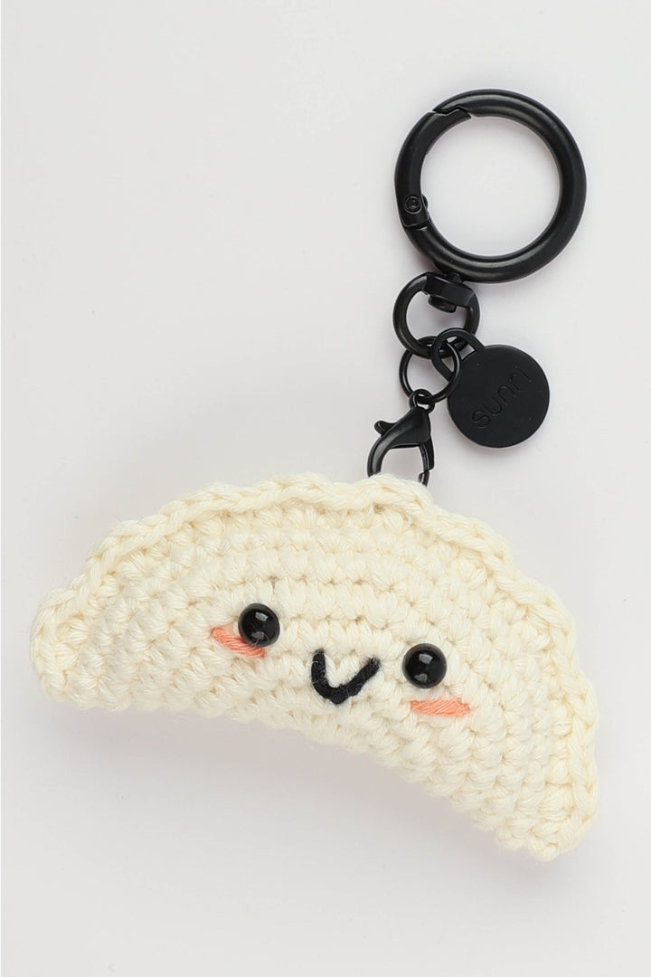 Crocheted Gyoza-shaped keychain with a face on a light gray background