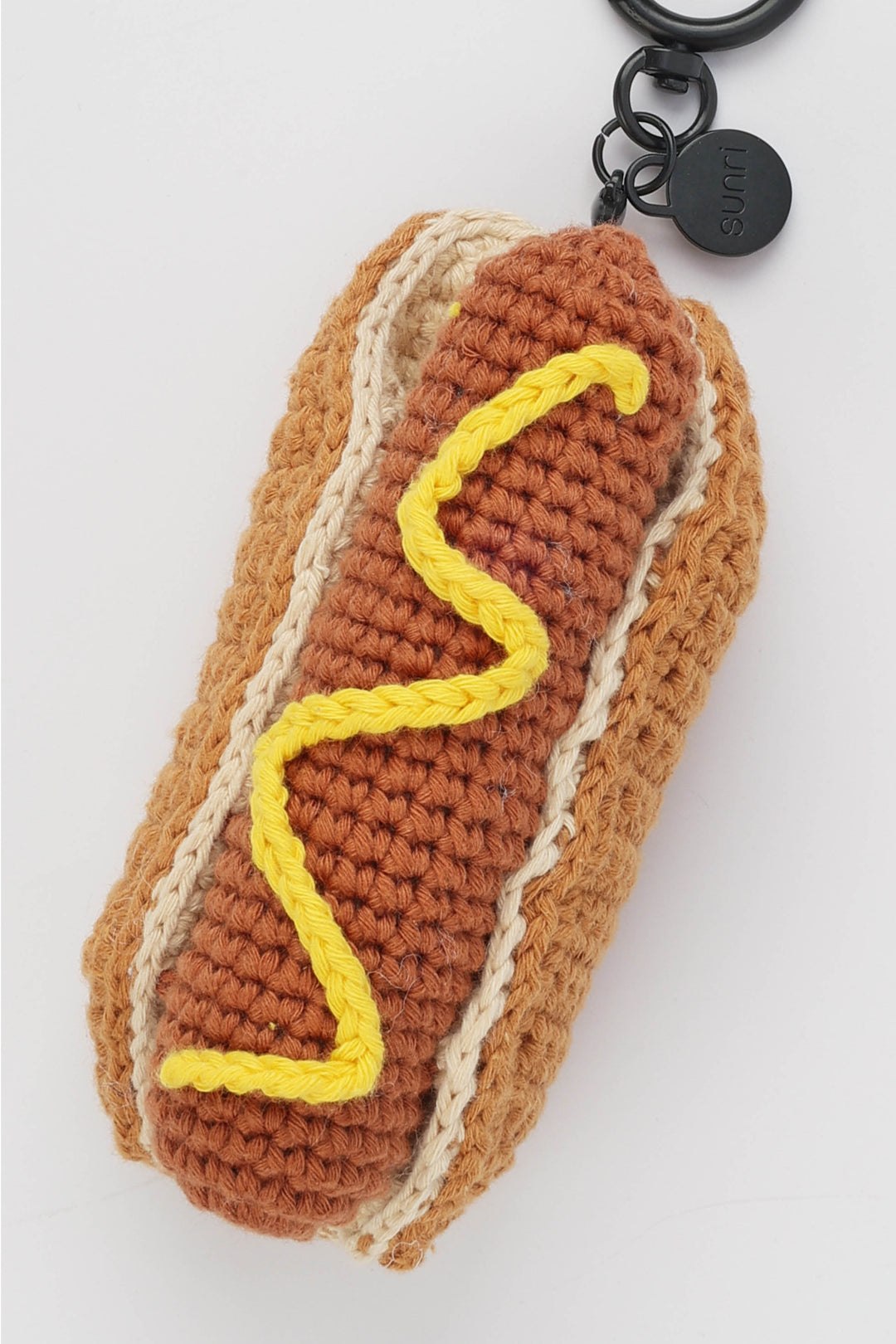 Crocheted hot dog keychain with mustard on a white background