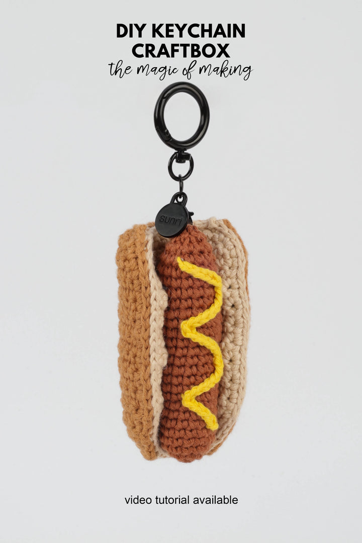 Crocheted hot dog keychain with mustard on a white background, featuring 'DIY Keychain Craftbox' text.