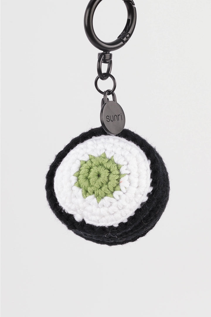Black and white crocheted keychain with a green center on a light gray background