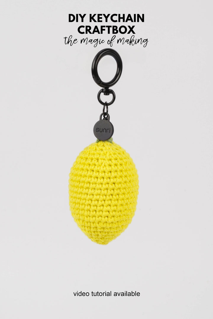 Yellow crocheted keychain with a black clip on a white background, featuring text about DIY keychain craftbox.