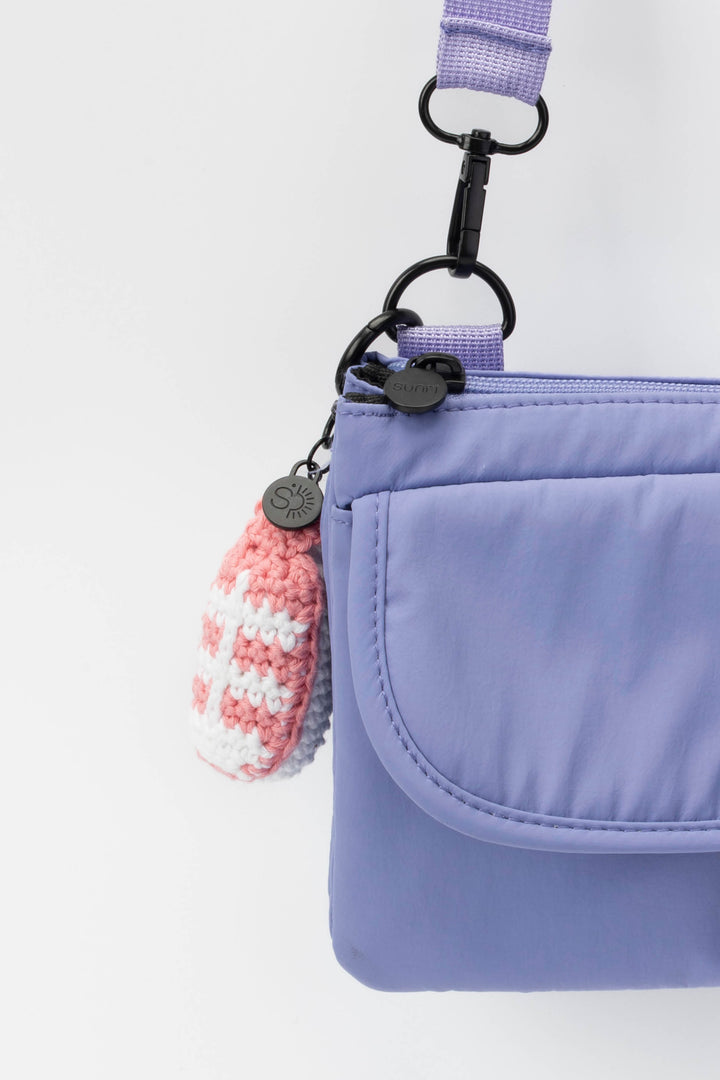 Purple crossbody bag with a pink and white crochet keychain on a light gray background