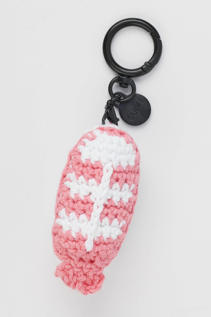 Pink and white crocheted keychain with a black ring on a light gray background