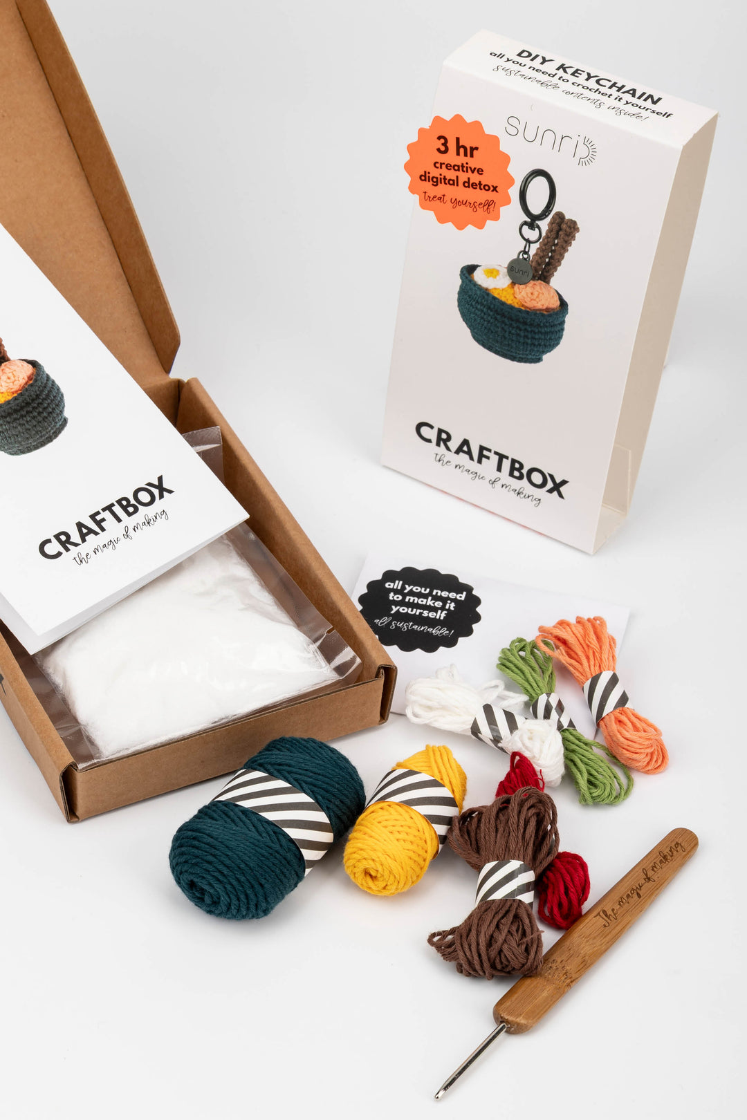 Craft kit with yarn balls, a needle, and a keychain in a box on a white background
