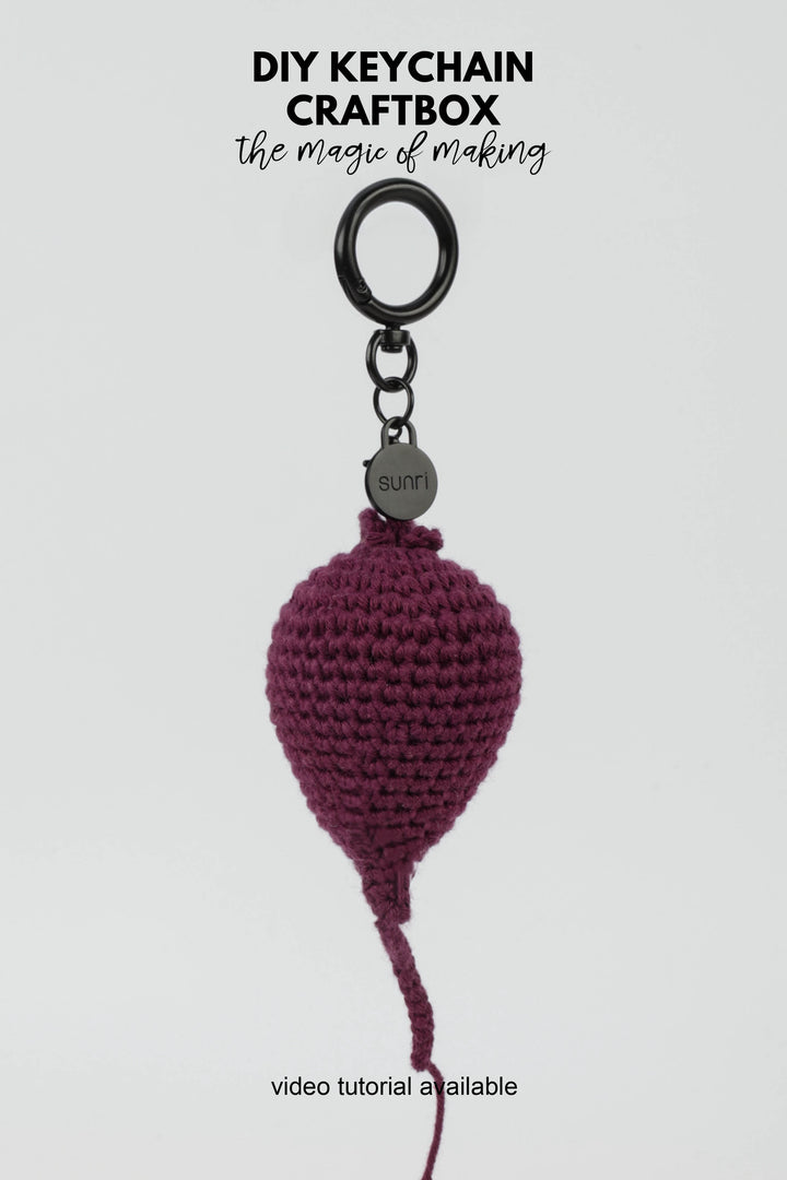 Crocheted keychain with a purple beetroot-shaped pendant on a white background, featuring text about DIY keychain craftbox.