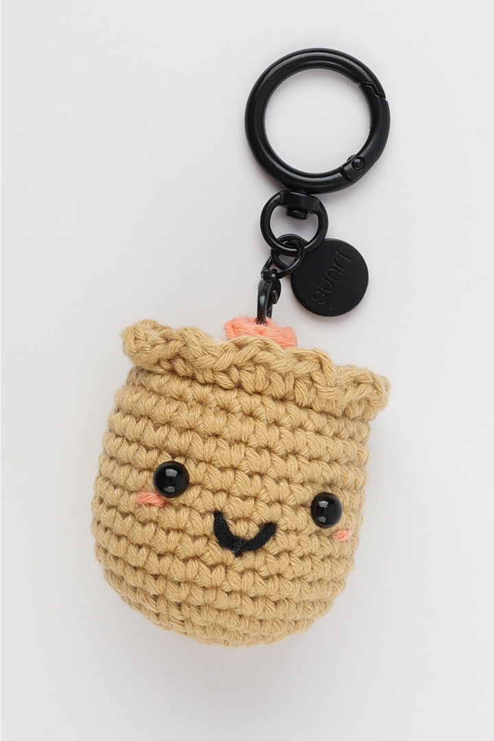 Crocheted beige bag charm with black eyes and a smile on a white background