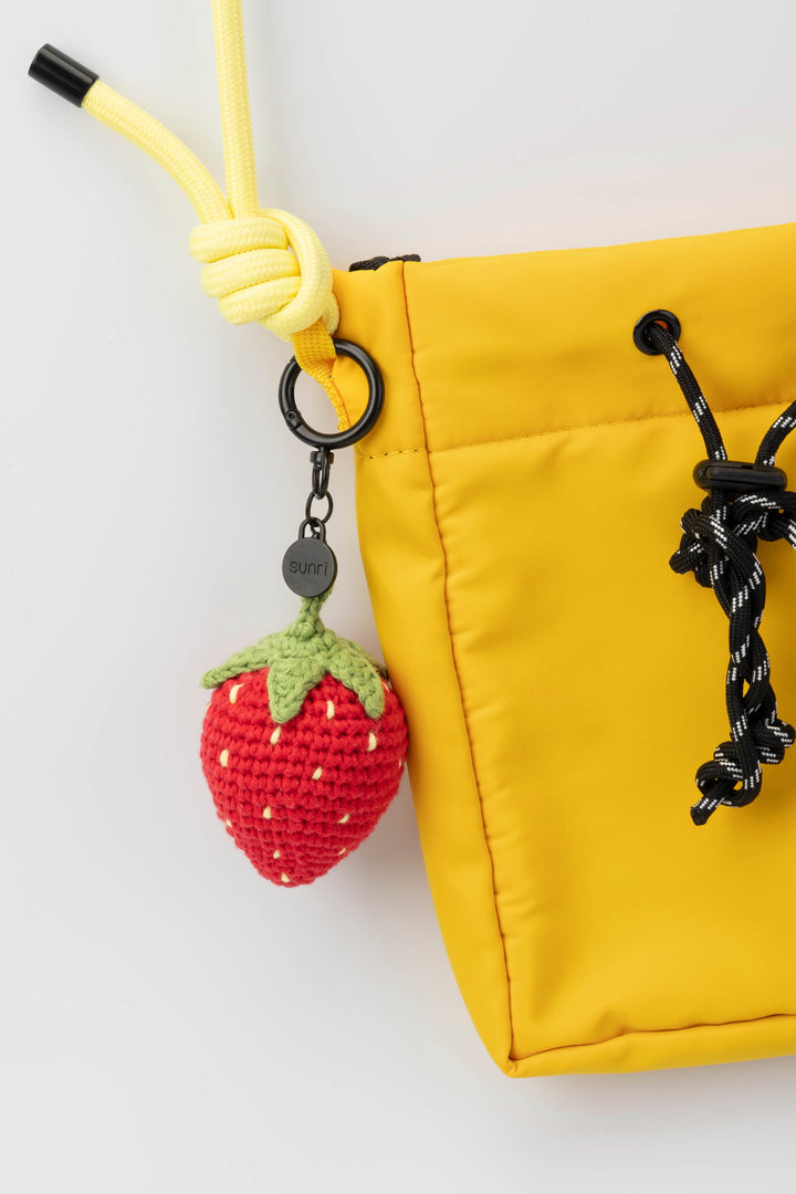 Yellow bag with a strawberry-shaped keychain on a white background