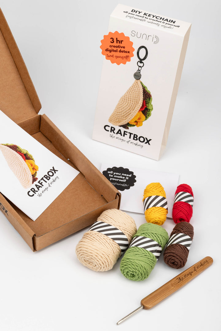 Craft kit with yarn, crochet hook, and keychain in a box on a white background