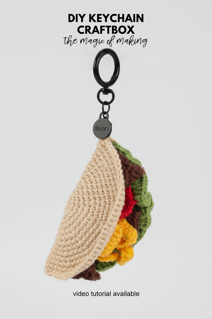 Crocheted taco keychain with a keyring on a light gray background, featuring text about DIY keychain craftbox.