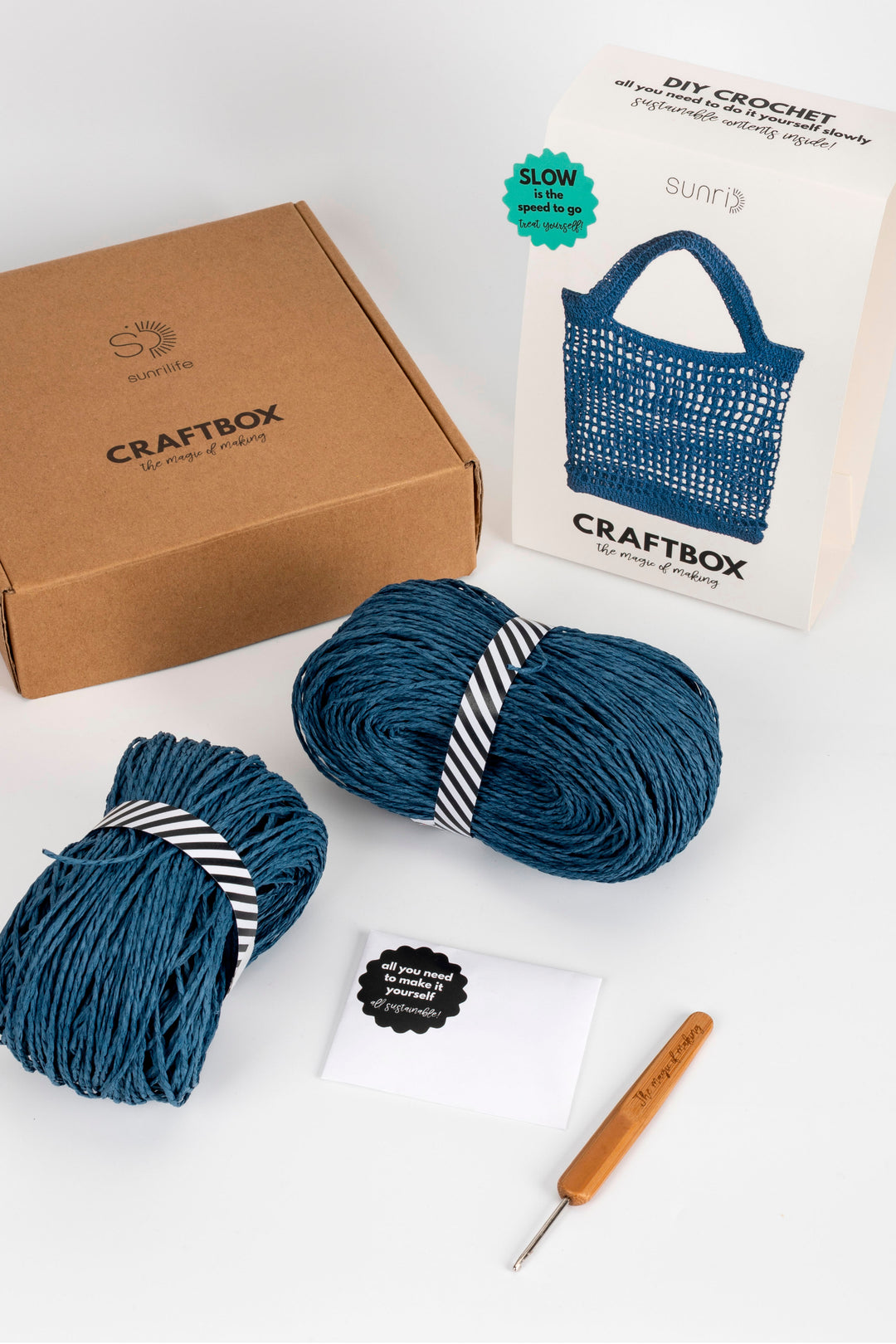 Craftbox with blue yarn, crochet hook, and pattern book on a white background