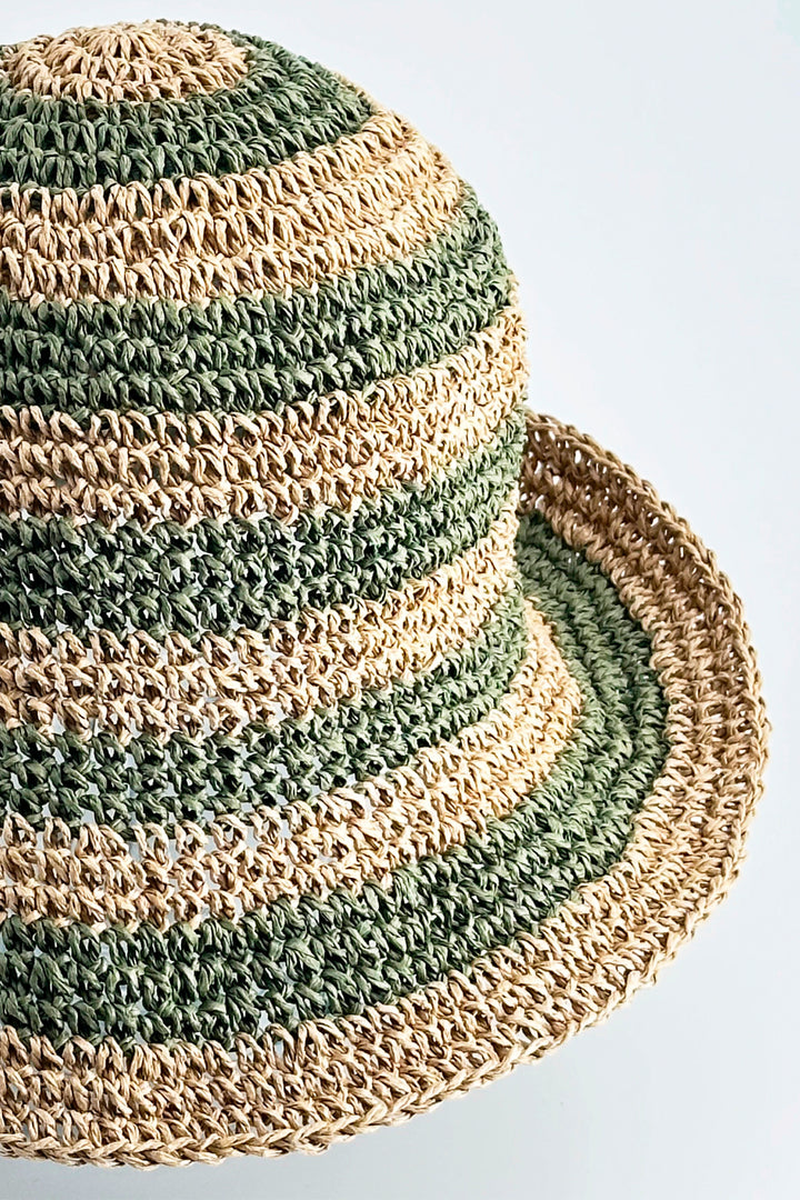 Close-up of a crocheted hat with green and beige stripes on a light gray background