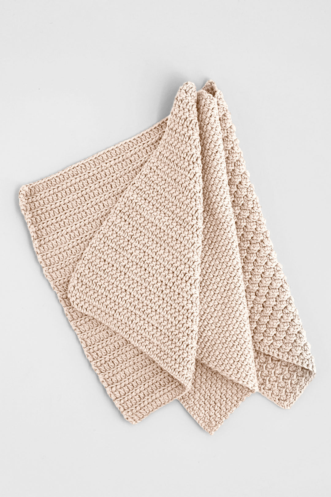 Three beige crocheted towels on a light gray background