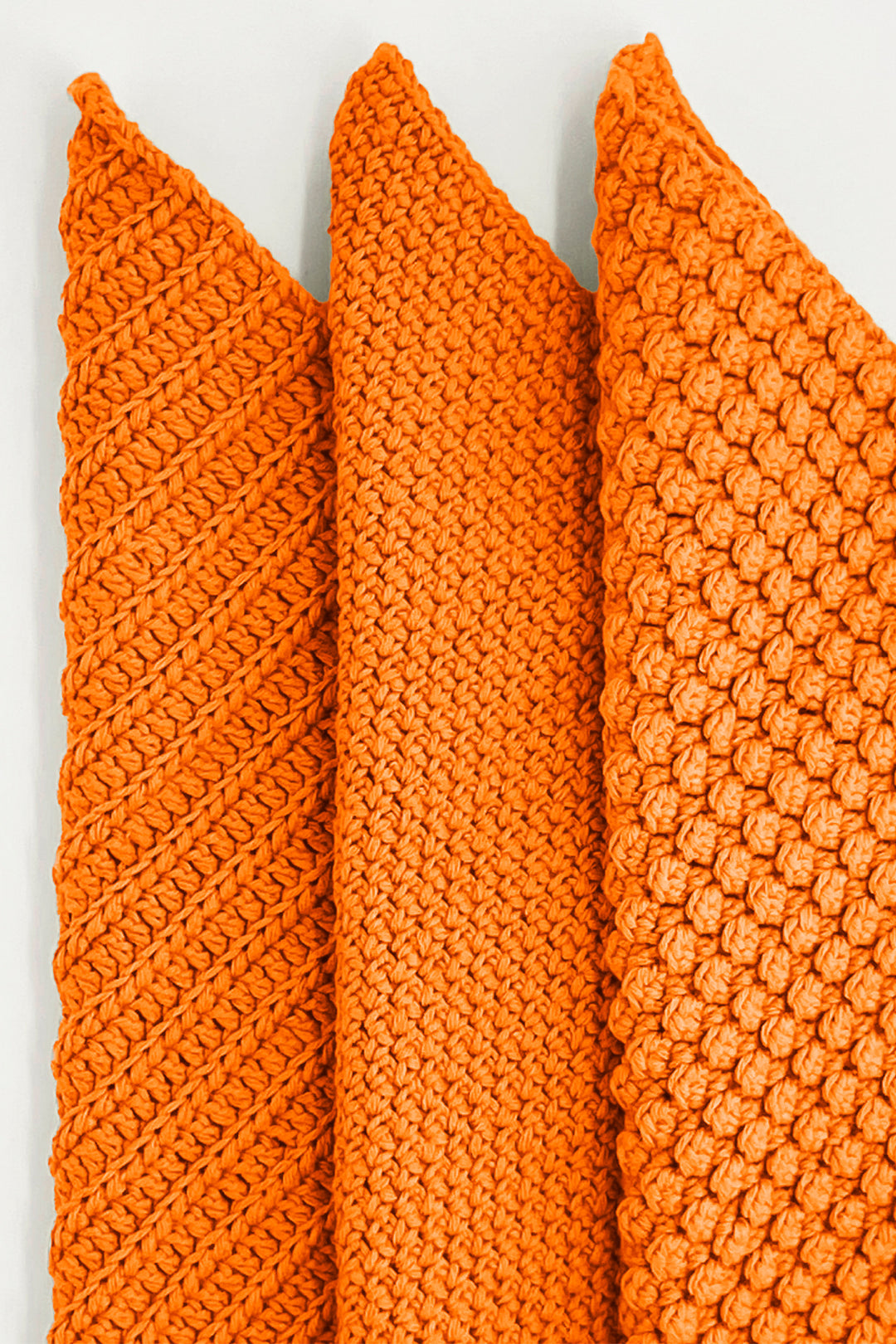 Three orange crochet towels of different patterns on a white background