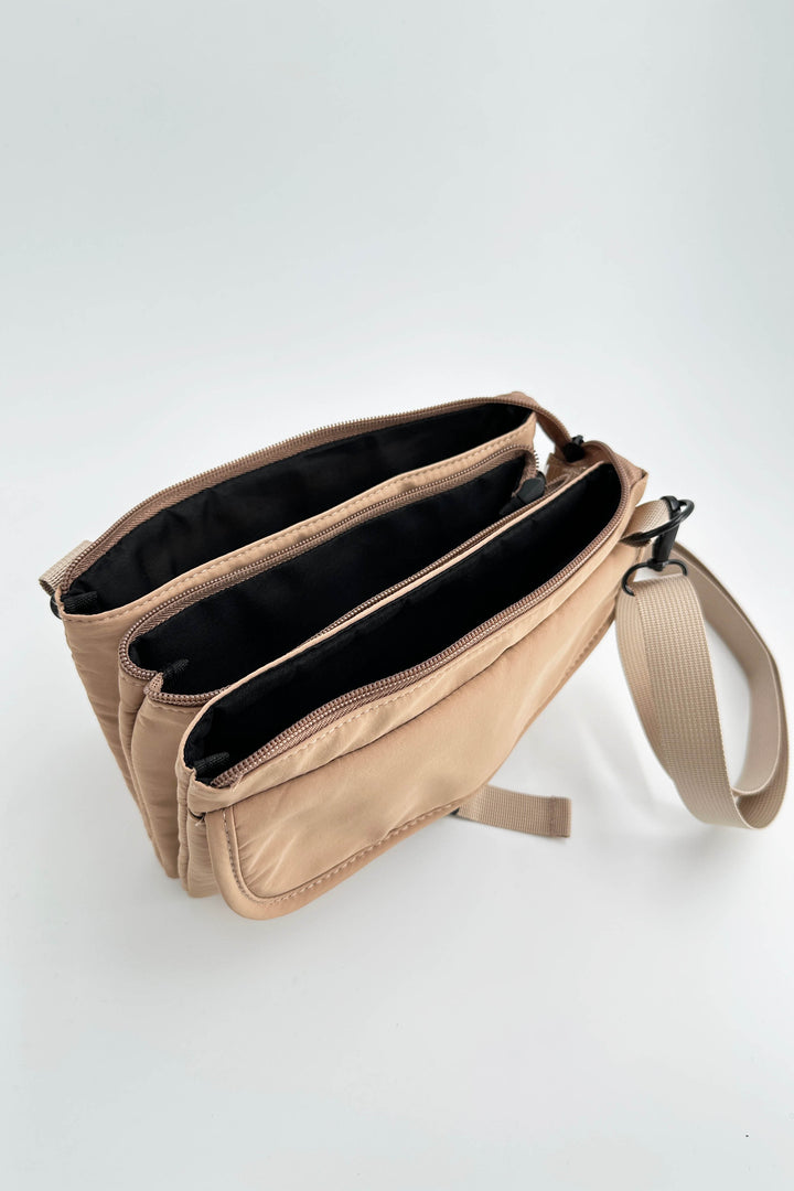 Beige crossbody bag with black interior on a light gray background