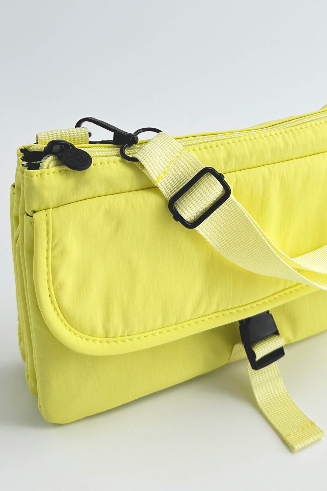 Yellow crossbody bag with black straps on a light gray background