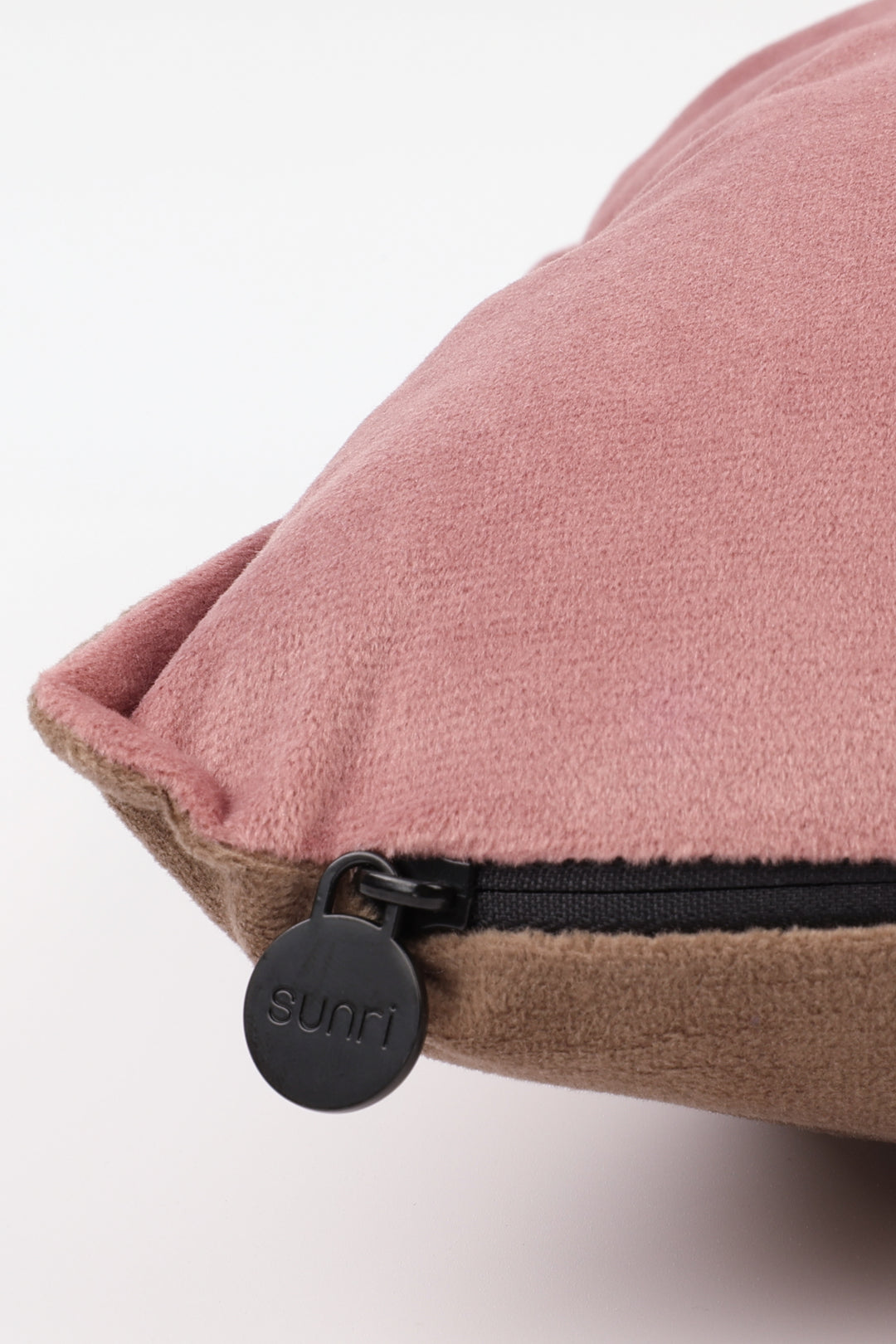 Close-up of a pink pillow with a black zipper and 'Sunri' label on a light background