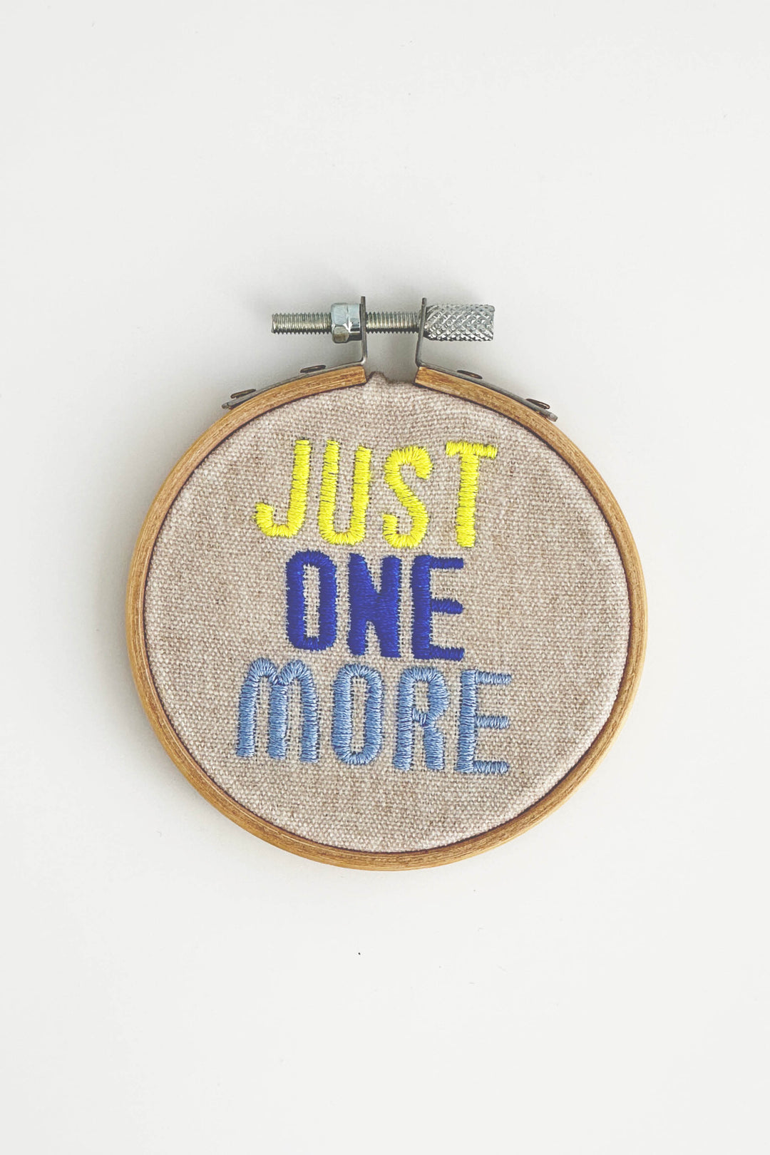 Embroidery hoop with 'Just One More' text on a white background