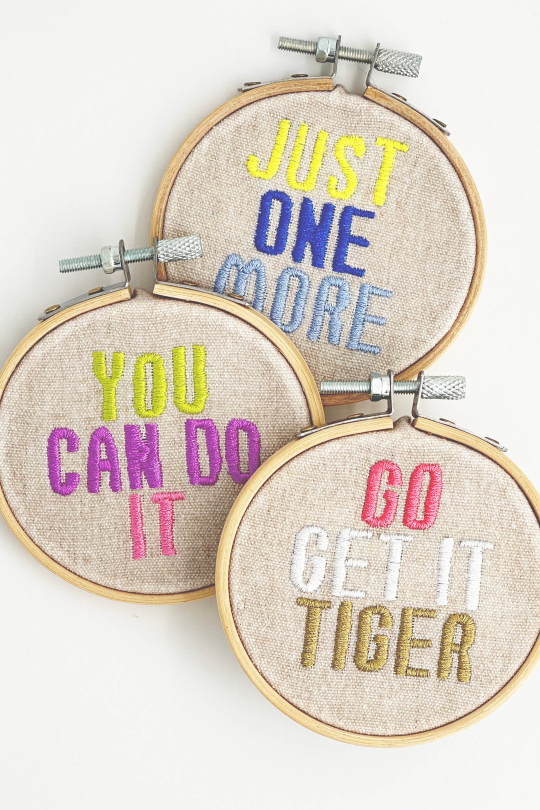 Three embroidery hoops with motivational phrases in colorful thread on a white background