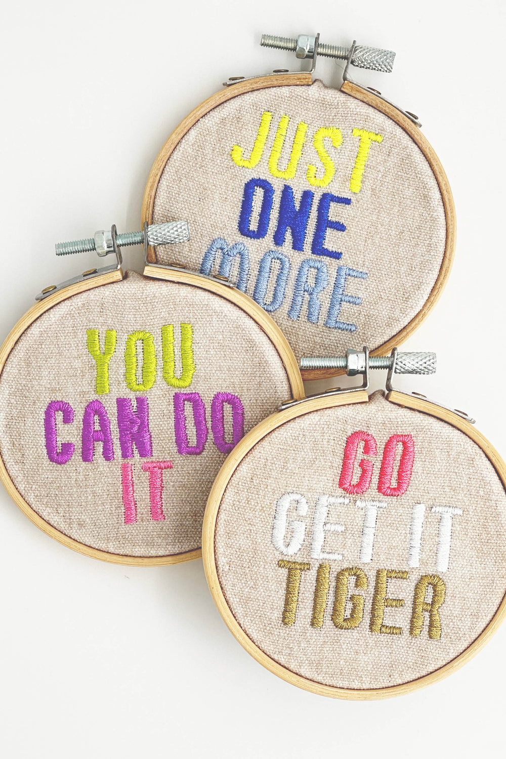 Three embroidery hoops with motivational phrases in colorful thread on a white background