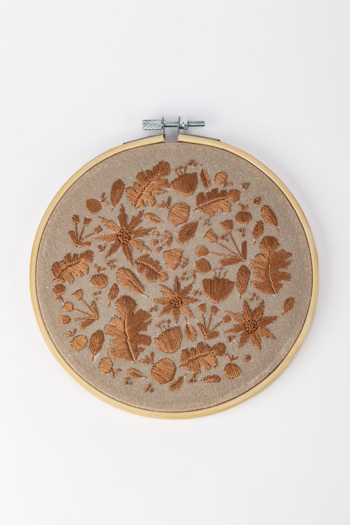 Embroidery hoop with floral pattern on a beige fabric against a white background
