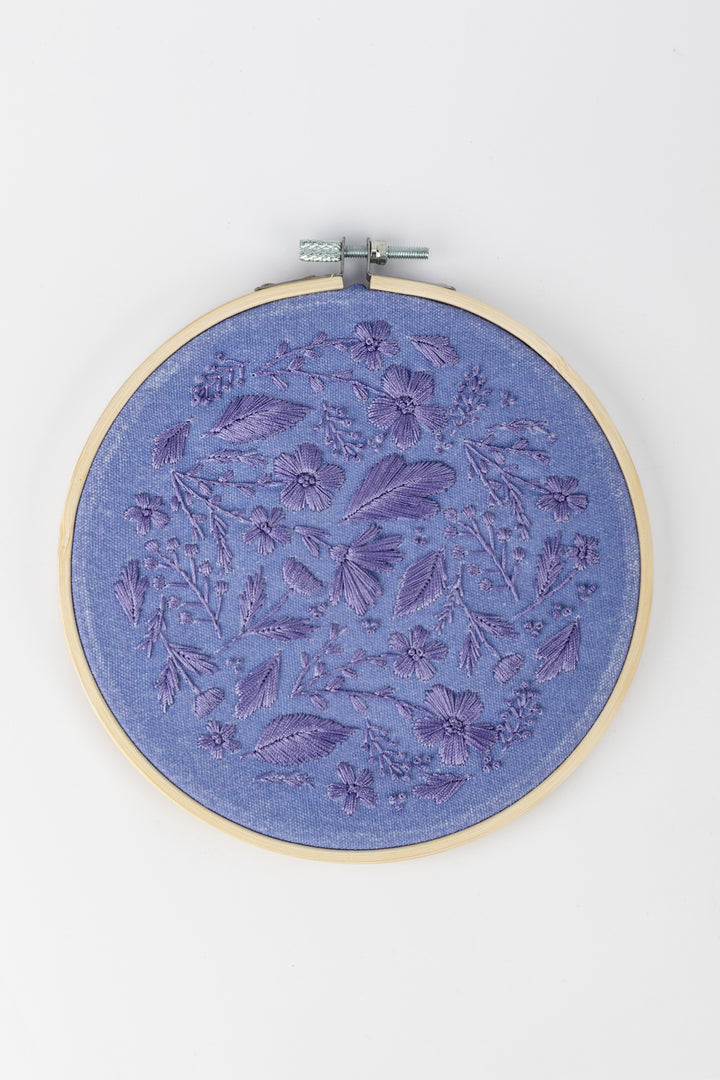Sunri Craftbox embroidery hoop with purple floral embroidery design on blue fabric on a white background
