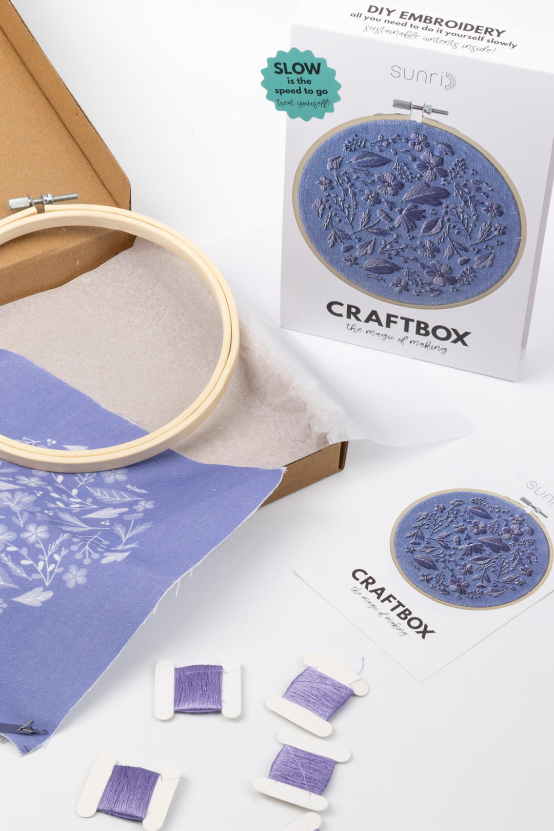 Sunri Craftbox DIY embroidery kit with wooden embroidery hoop, purple threads, floral design fabric and packaging box on a white background