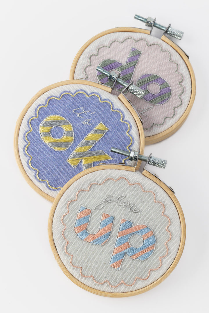 Three embroidery hoops with colorful text designs on a white background