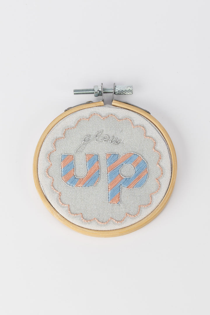Embroidery hoop with 'glow up' text on a white background