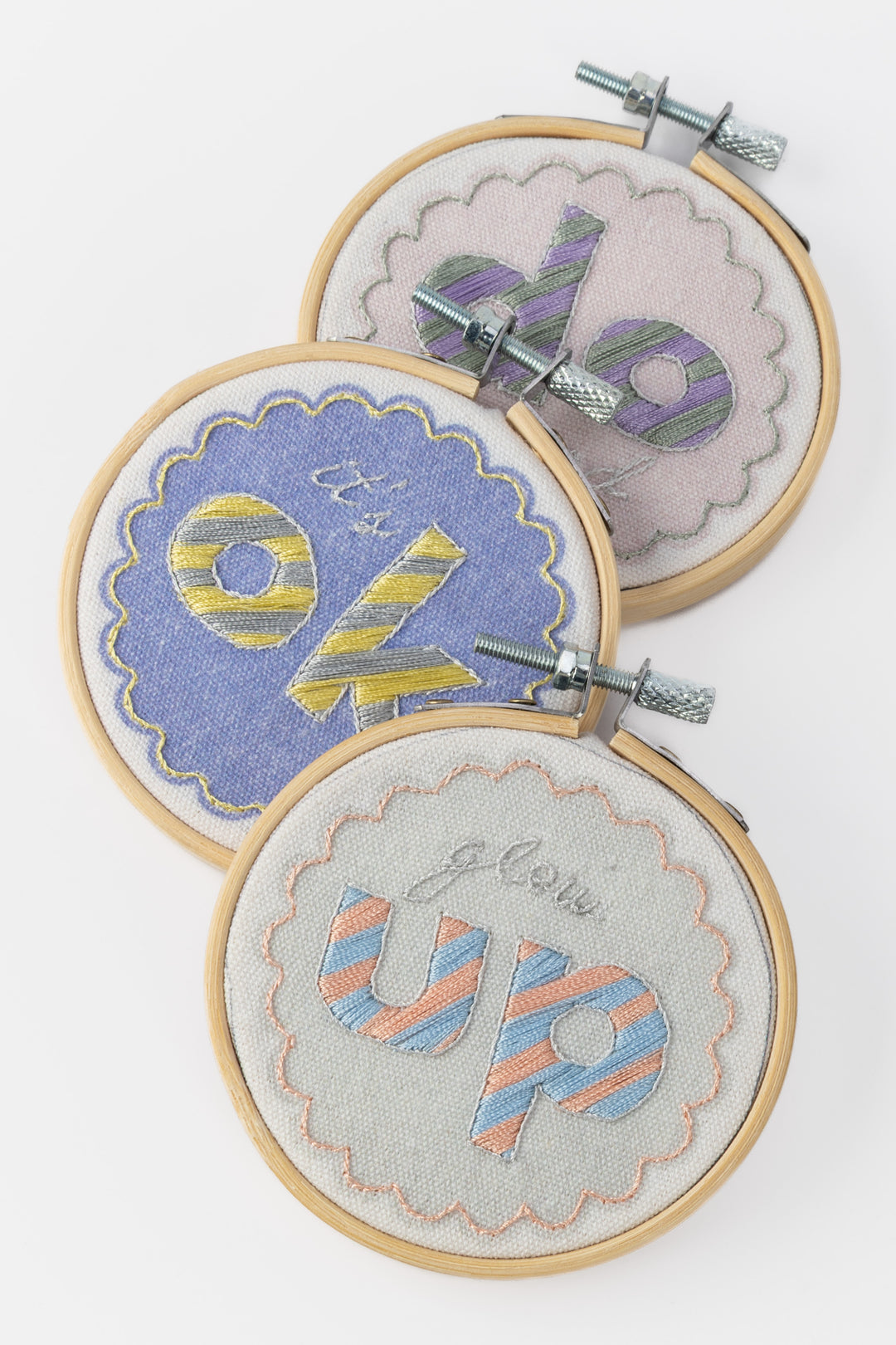Three embroidery hoops with colorful text designs on a white background