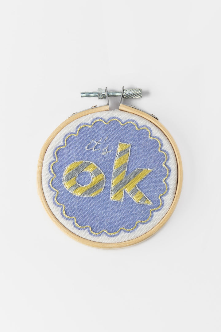 Embroidery hoop with 'it's ok' text on a blue background