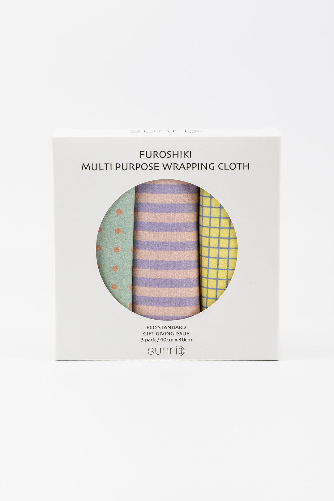 A boxed set of three folded wrapping cloths visible through a circular window on a white box. The cloths show pastel patterns: mint green with orange dots, lavender and pink stripes, and yellow grid.