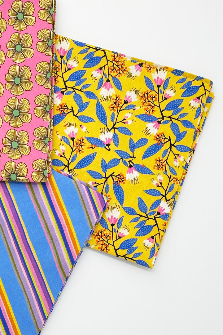 folded furoshiki wrapping cloth with yellow floral print next to blue striped cloth