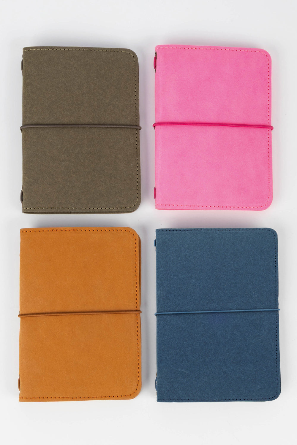 Four colorful passport size sketch journals (green, pink, orange, blue) arranged in a 2x2 grid on a white background.