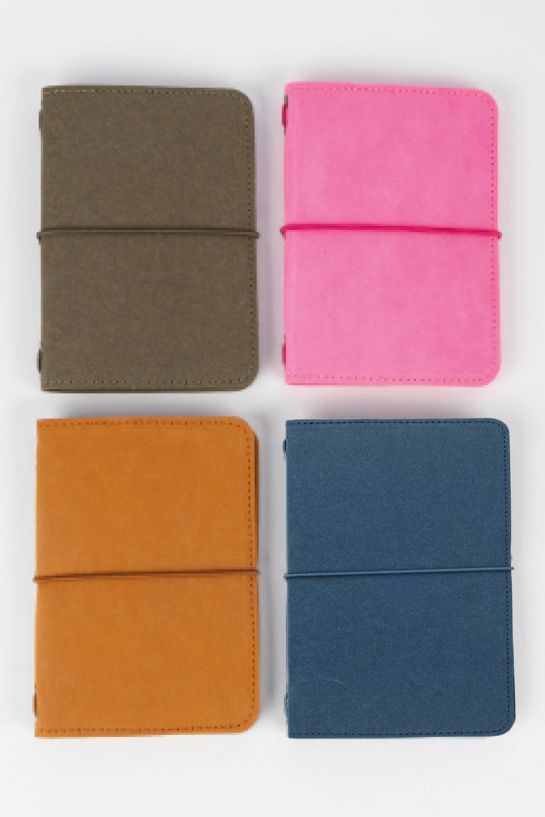 Four colourful passport size sketch journals (green, pink, orange, blue) arranged in a 2x2 grid on a white background.
