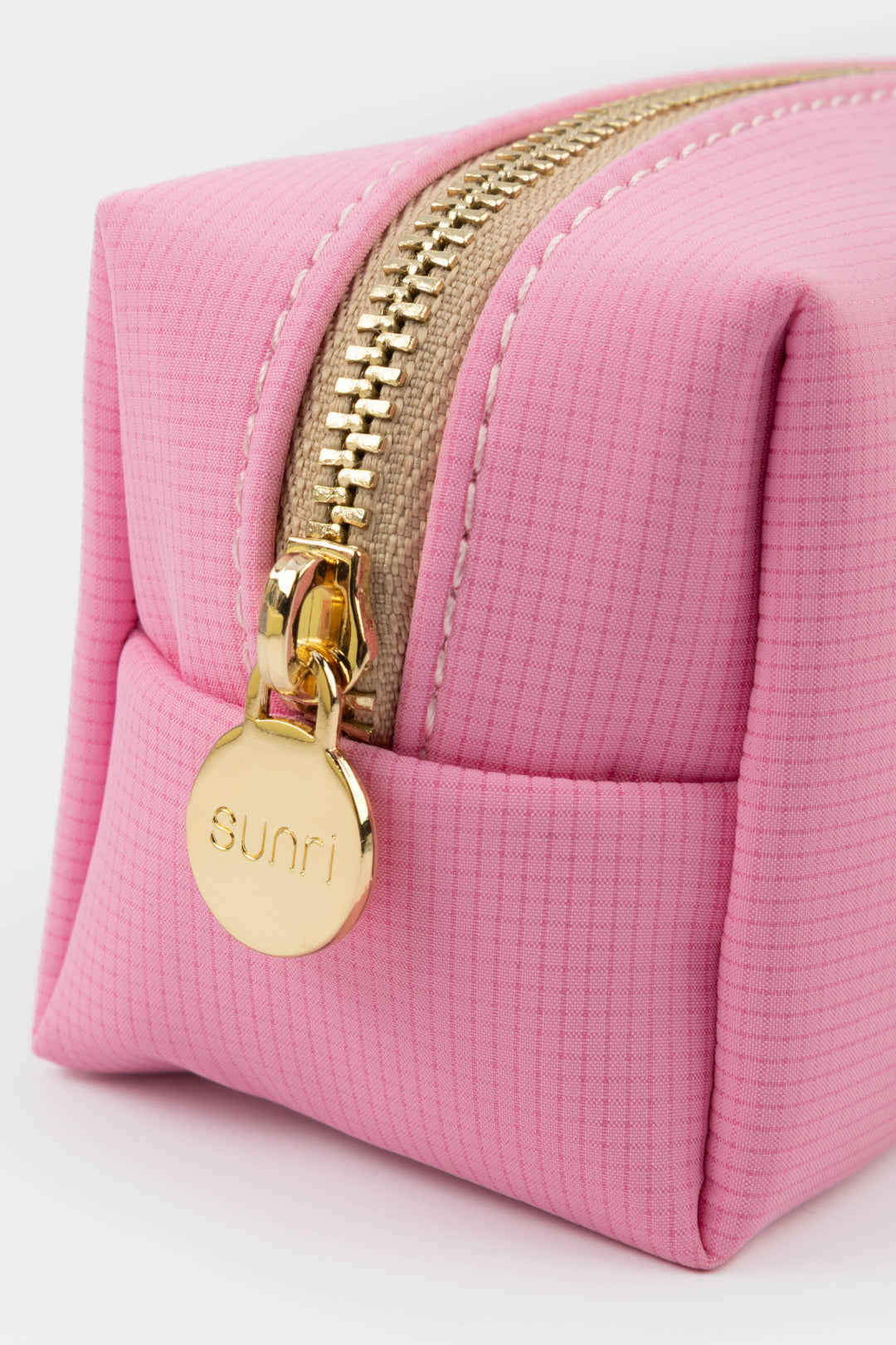 Pink pouch with gold zipper and 'sunri' tag on a light background