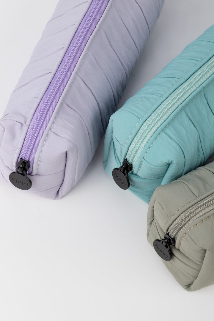 Three fabric pouches in gray, purple, and teal on a white background