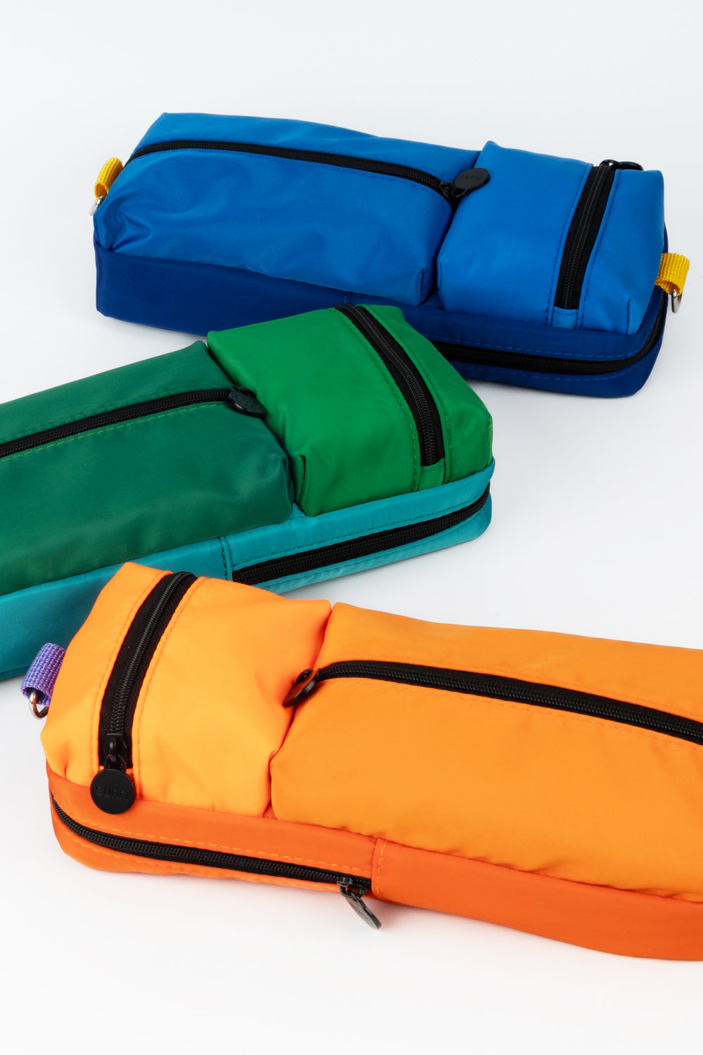 Three colourful pencil cases in blue, green, and orange on a white background
