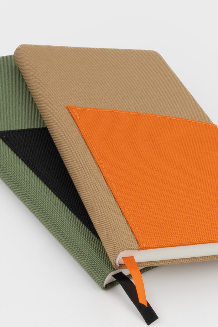 Two pocket notebooks stacked showing brown cover with orange pocket and green cover with black pocket
