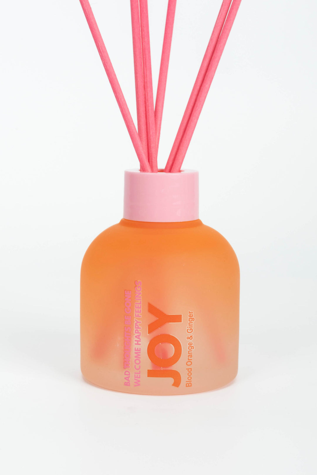 Orange diffuser bottle with pink cap and reeds on a white background
