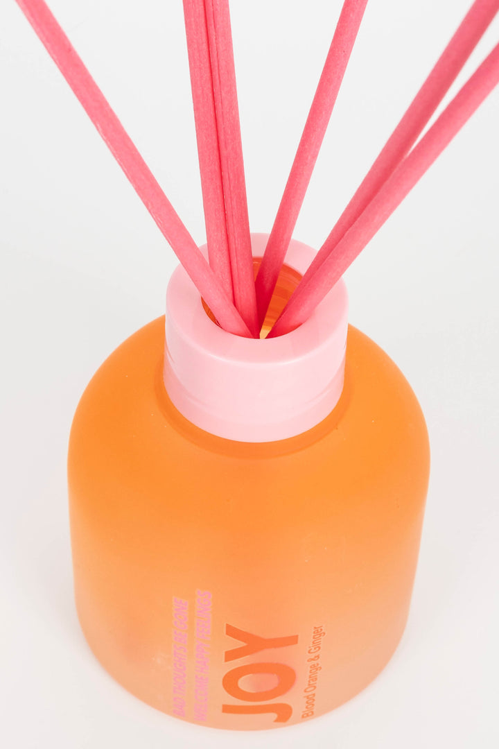 Orange diffuser bottle with pink reeds on a white background