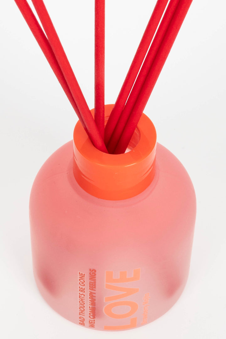 Pink diffuser with orange cap and red sticks on a white background