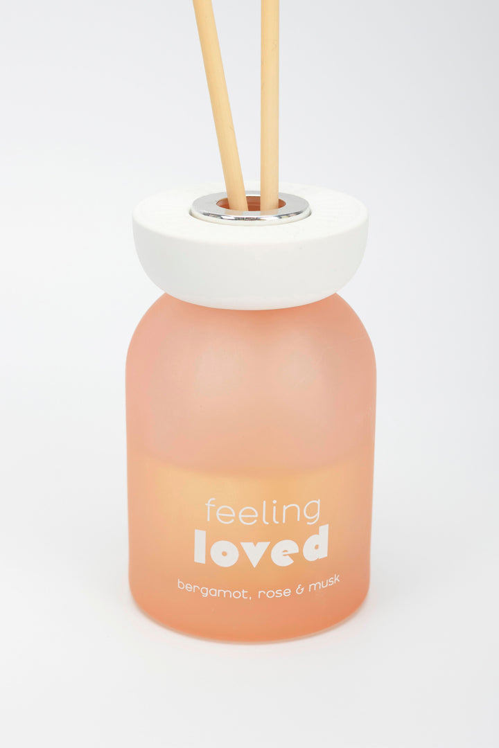 Diffuser bottle labeled 'feeling loved' with wooden sticks on a white background