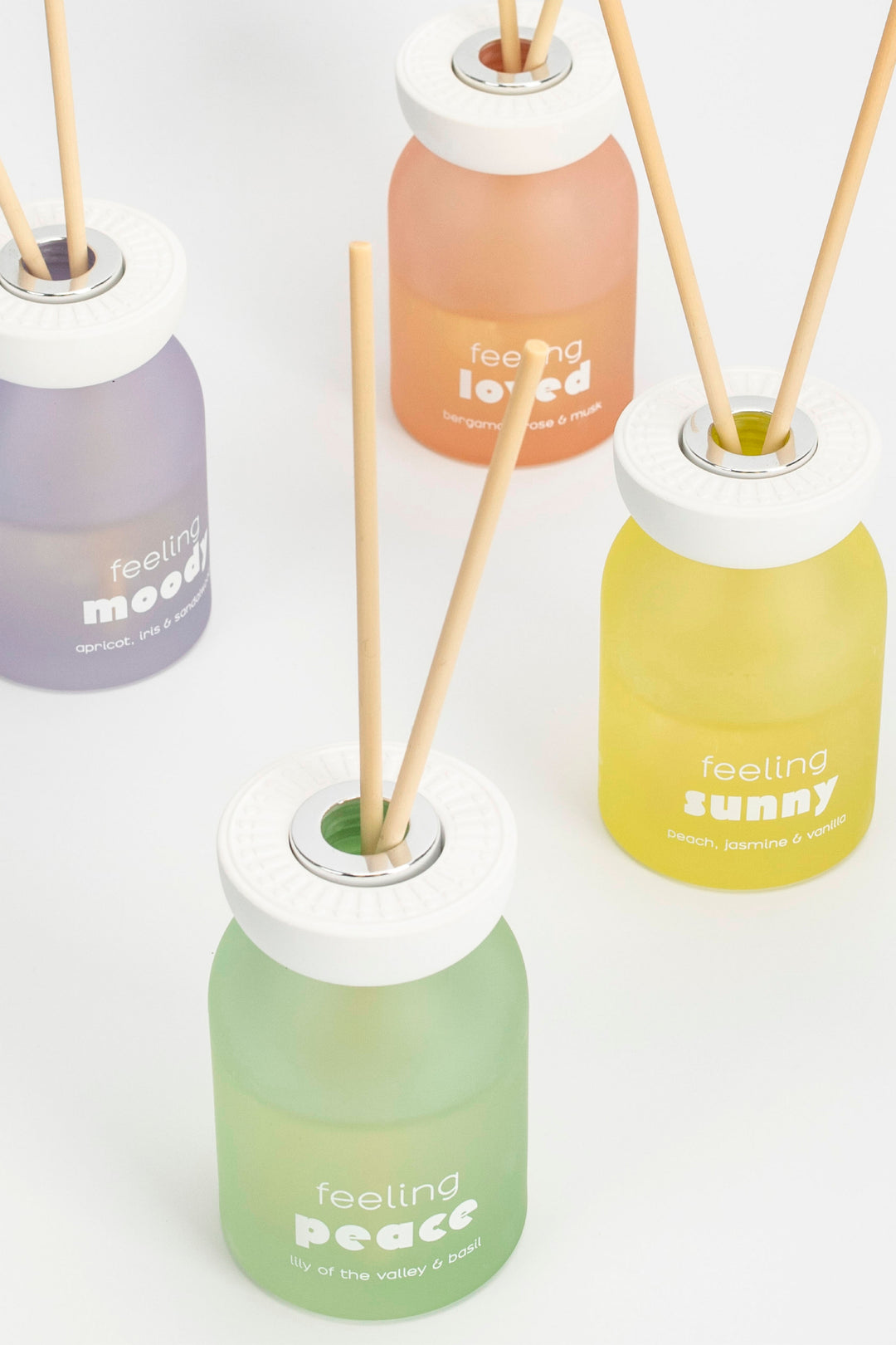 Four diffuser bottles with sticks labeled 'feeling loved', 'feeling peace', 'feeling sunny', and 'feeling good' on a white background.